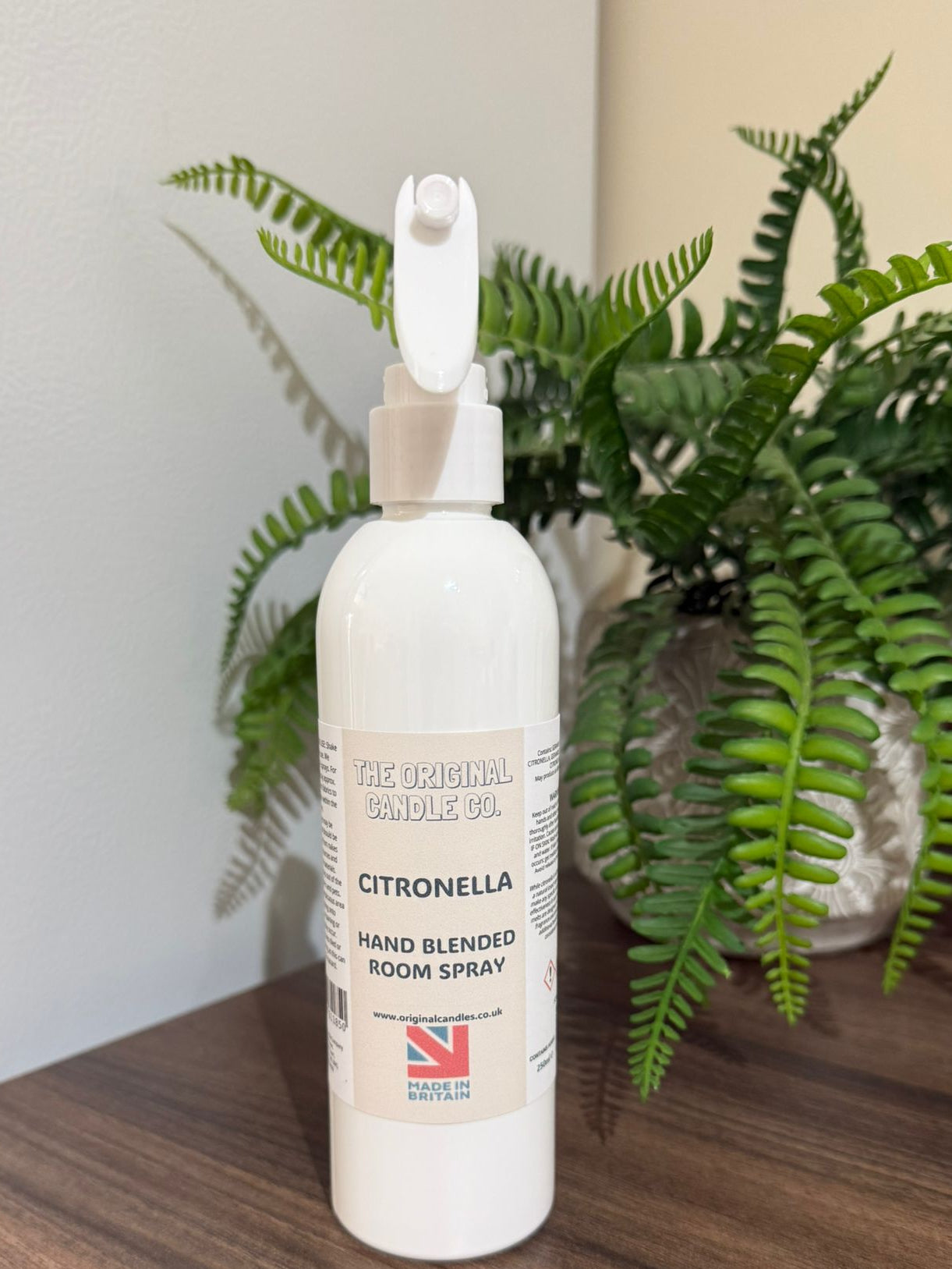 White bottle of Citronella hand blended room spray on a wooden surface with a plant in the background