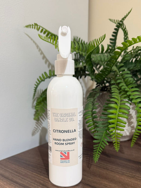 White bottle of Citronella hand blended room spray on a wooden surface with a plant in the background