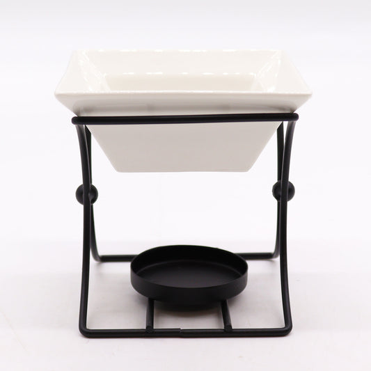 A side perspective of The Original Candle Company’s modern square ceramic oil burner, framed in sleek black metal. Designed to enhance wax melting and essential oil diffusion, its contemporary aesthetic adds refinement to any space.