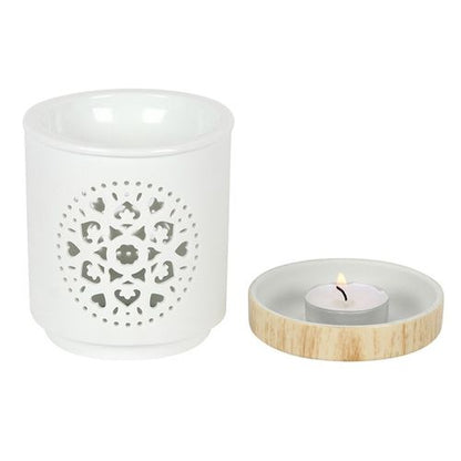 This white ceramic oil burner features a cutout mandala design with a wood-effect ceramic base. Place fragrance oil or wax melts into the built-in dish with a standard tealight inside to fill the home with calming fragrance. Image depicts the wood effect base showing where the tealight sits.
